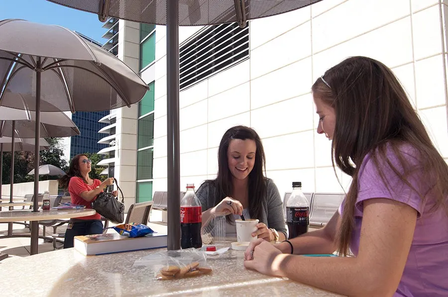 TWU Houston students eat lunch outside on covered tables. 