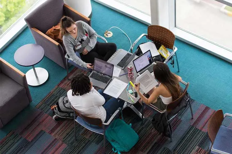 Students sit together in a common area with laptops and notes