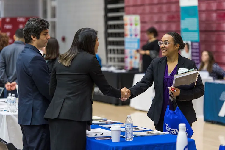 A student shakes hands with a potential employer at a job fair booth