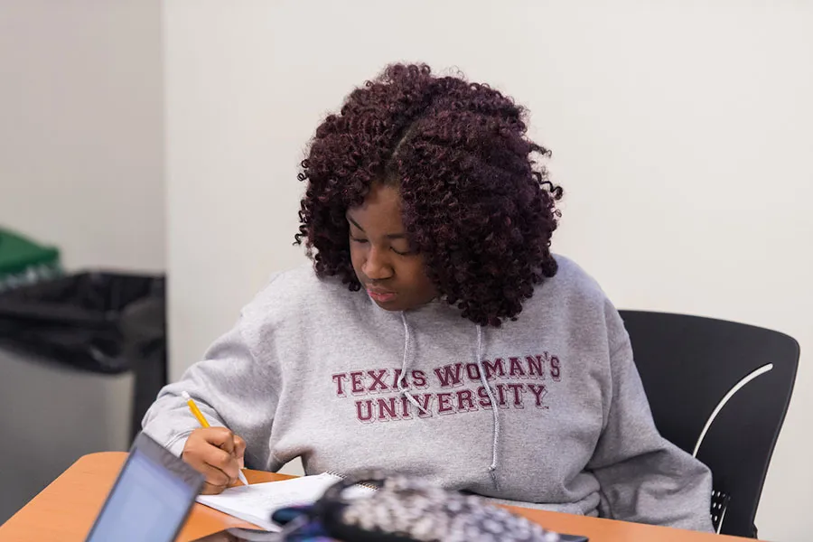 A young woman in a TWU sweatshirt takes notes for a class
