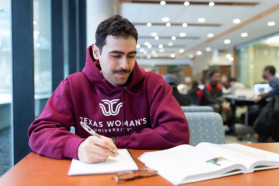 A male TWU student in a TWU hoody studies a textbook