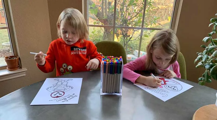 A young boy and a young girl coloring TWU themed coloring pages at a dining table.