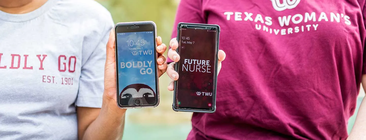 Two students in TWU shirts hold up their phones withTWU themed wallpapers on the screens.