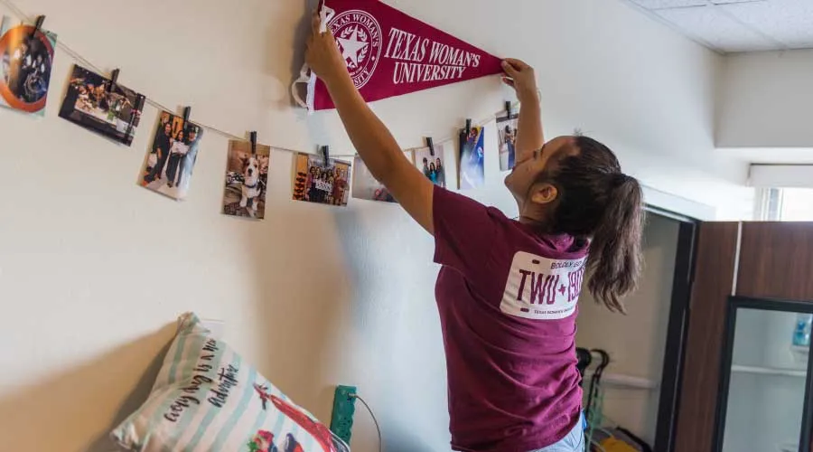 A TWU student puts up a pennant on her dorm room wall.