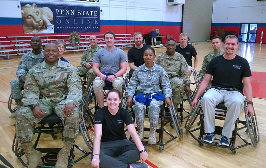 APE scholars sit with a group of wheelchair-bound military veterans on a basketball court 