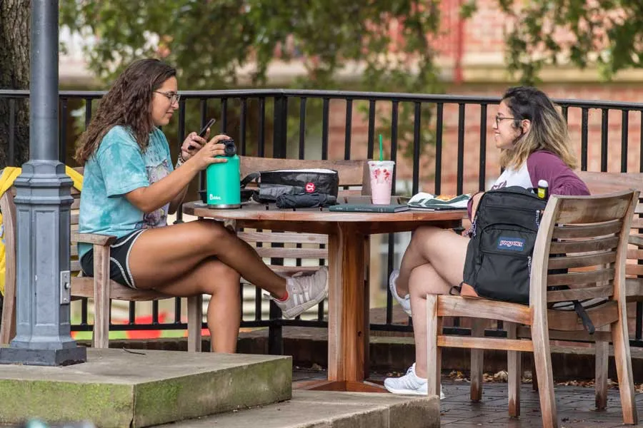 Two TWU students sit at a table outdoors and relax on the Denton campus.