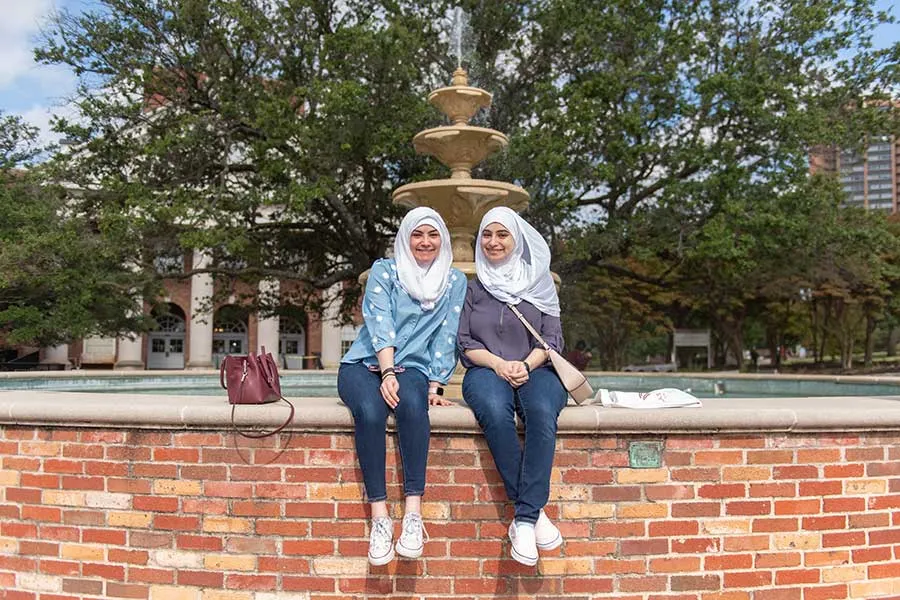 Two TWU students sit and talk at the Denton campus fountain on a sunny evening.