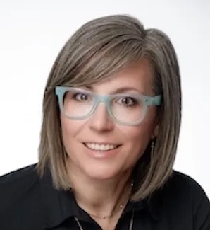 Woman with short blond hair and green glasses smiles directly at the camera