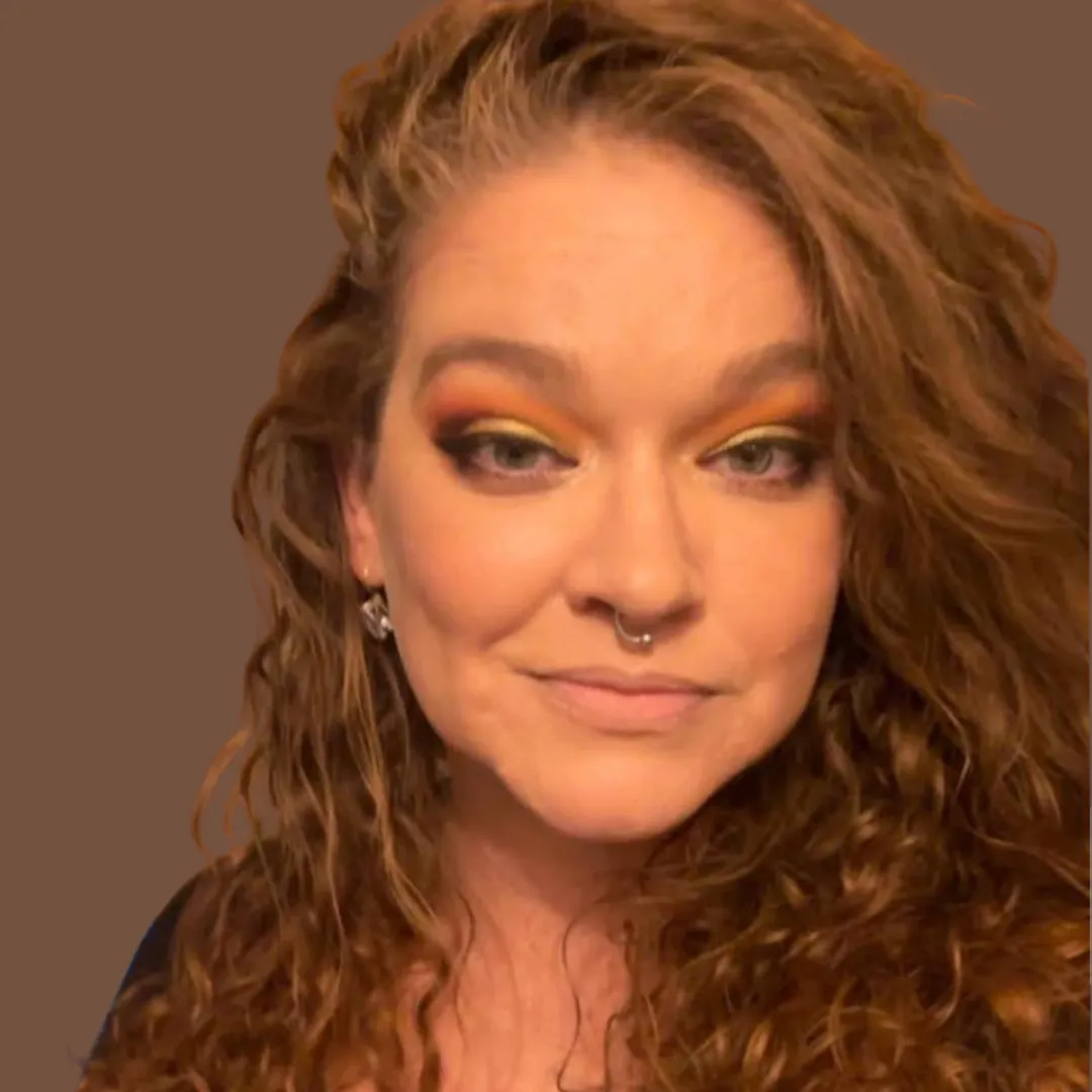 woman with long hair looks directly at camera in front of reddish background
