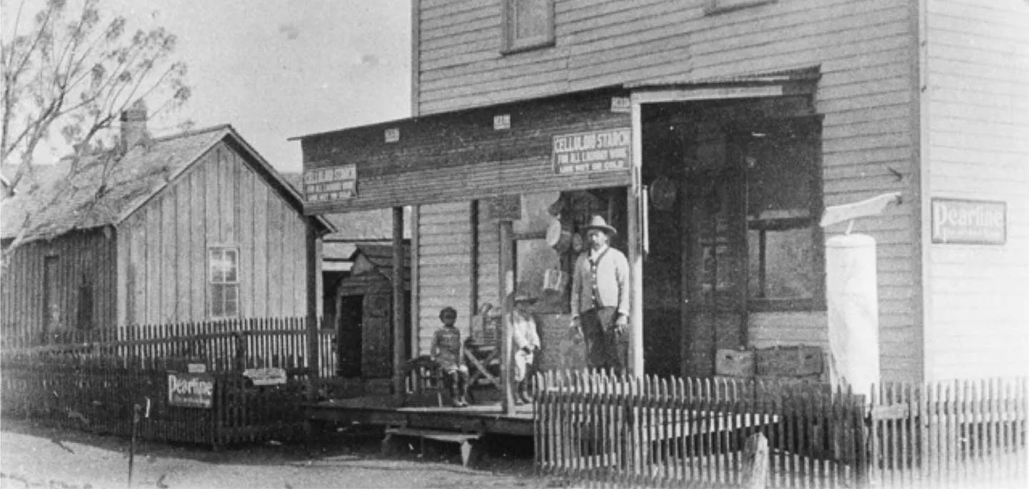 A black and white photo of a man and two children standing on the porch of a business in Quakertown in Denton, TX.