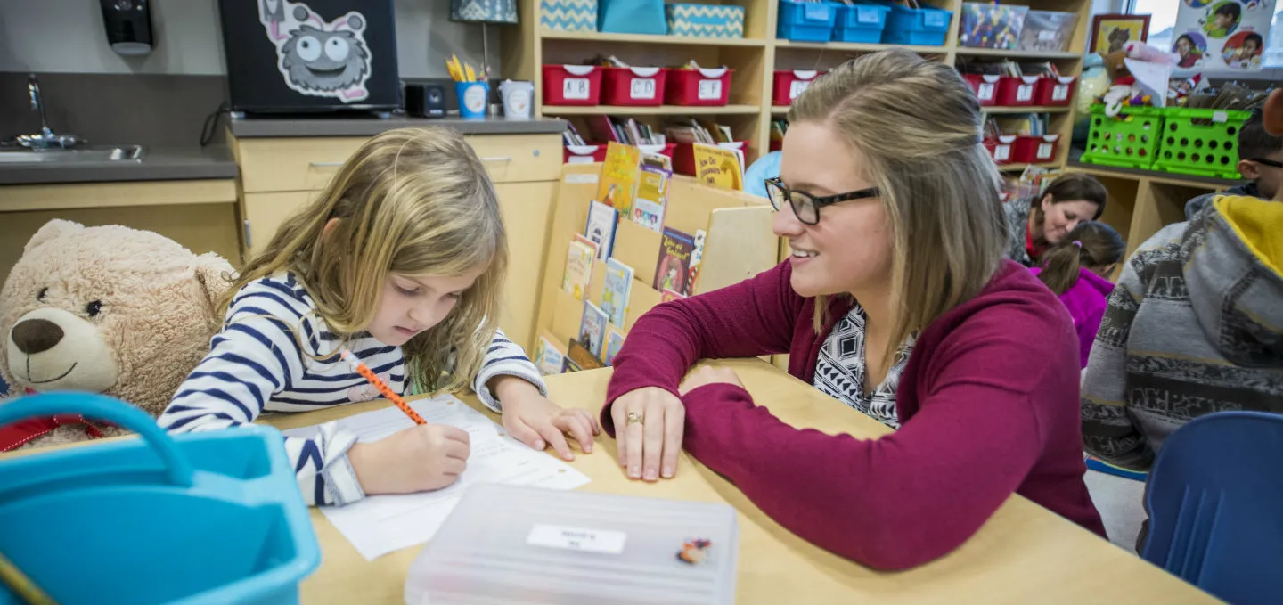 Student teacher assist a young girl with reading homework.