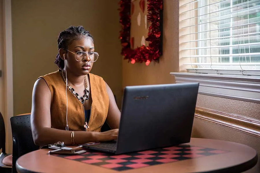 A student with headphones sits at a table in front of a laptop