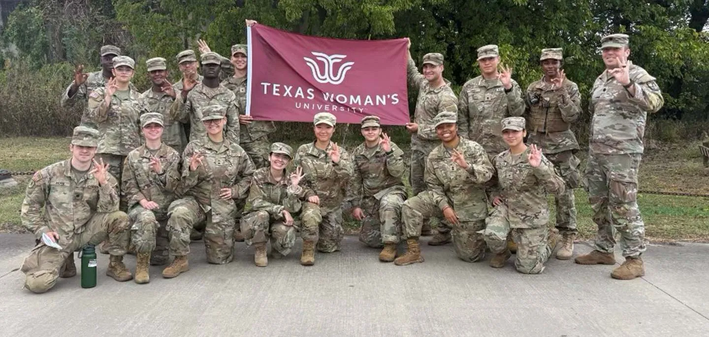 TWU ROTC students holding up the TWU hand sign and flag