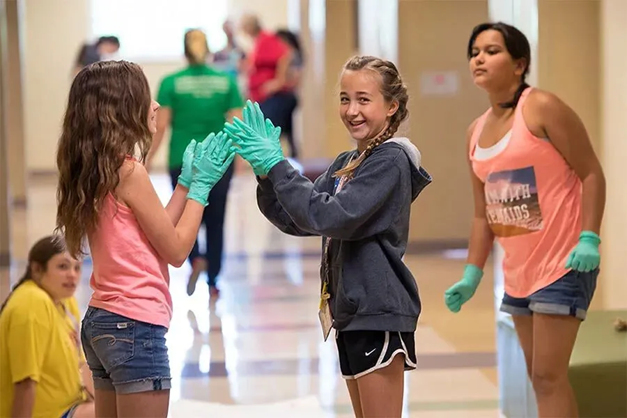 Middle school aged girls in a school setting wearing gloves and prepping for a science experiment.