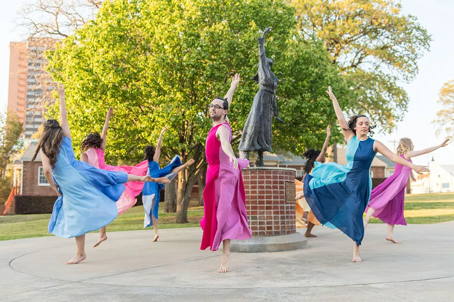 Dancers in rainbow colors perform near a statue on campus