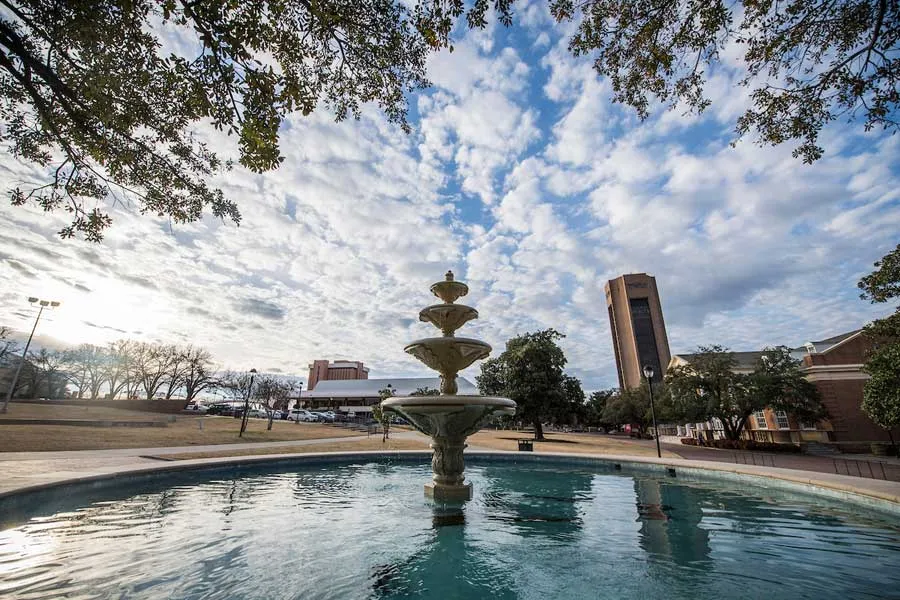 The TWU Fountain in the center foreground, with a cloudy sky, ACT and the Student Union in the background.