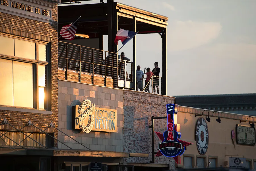 Discover Denton, LSA Burgers, and Beth Marie's storefronts on the downtown Denton Square at dusk.