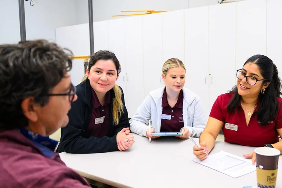 three TWU students sit at a table with a Stroke Center client