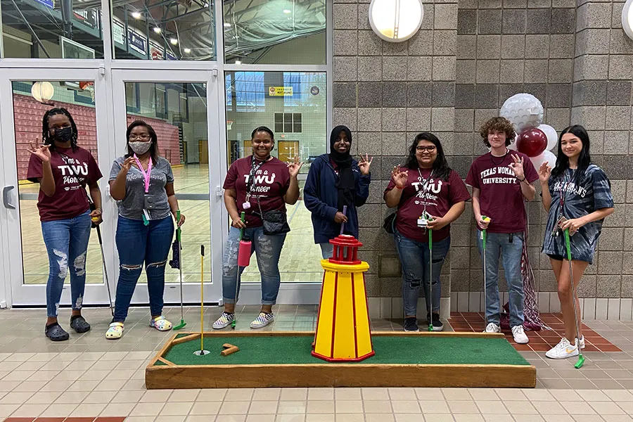 SGA members make the TWU hand sign in front of a mini golf putting green