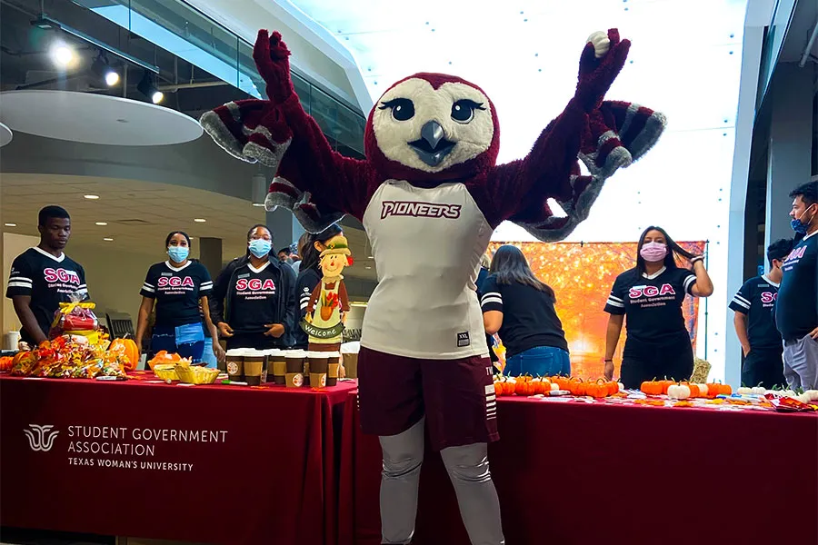 TWU. mascot Oakley holds up a tiny pumpkin in front of the SGA fall table