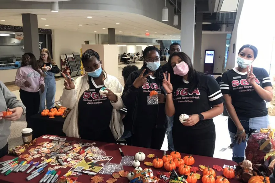 SGA members in protective face masks pose in front of a fall table as they make the TWU hand sign