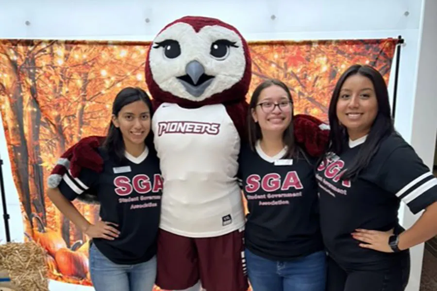 3 SGA members pose with TWU mascot Oakley in front of a fall themed backdrop
