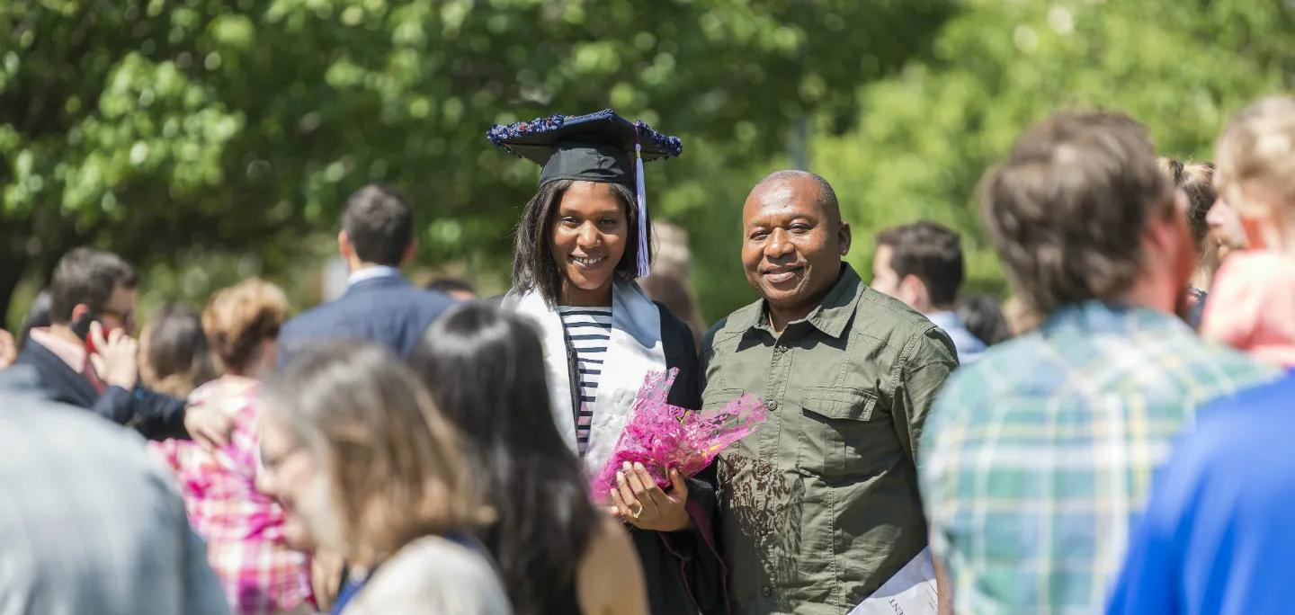 A TWU graduate stands out in the crowd in a cap and gown with her father by her side on TWU's Denton campus.