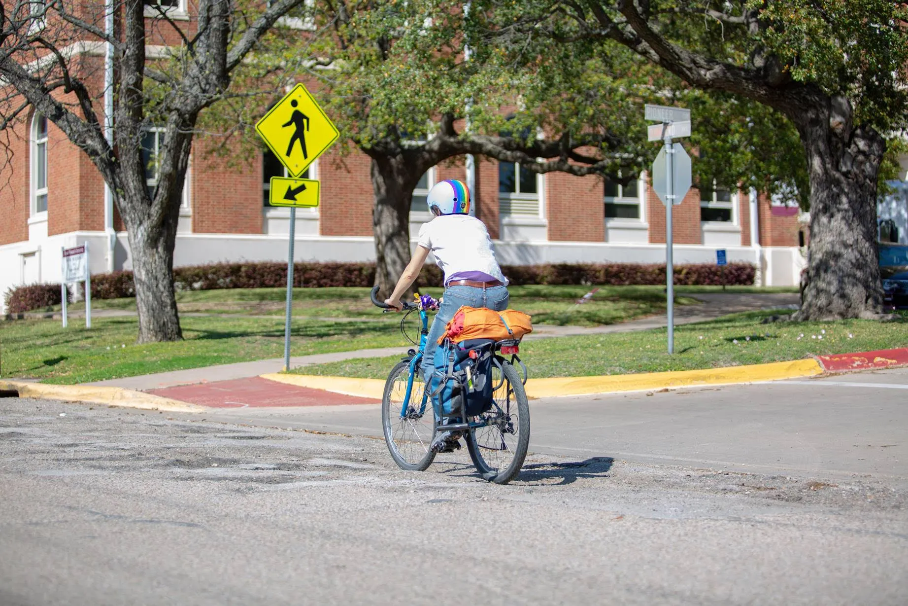 University employee riding their bicycle to work along Oakland Drive in front of the Music/Margo Jones building