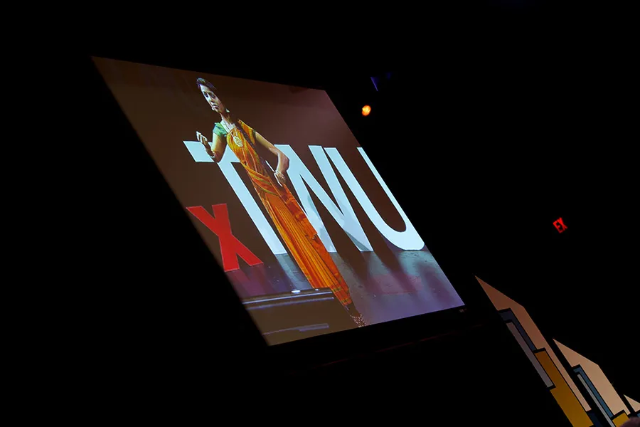 A woman in traditional east Indian garb stands on a stage in front of a TEDxTWU sign