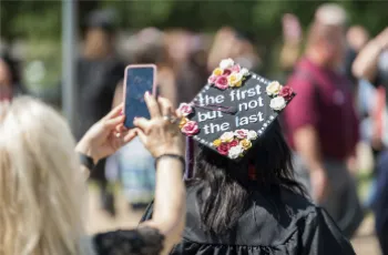 Student with decorated mortar board graduation cap stating 'the first...but not the last'.