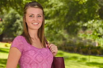 A smiling woman outside in a pink short sleeved shirt