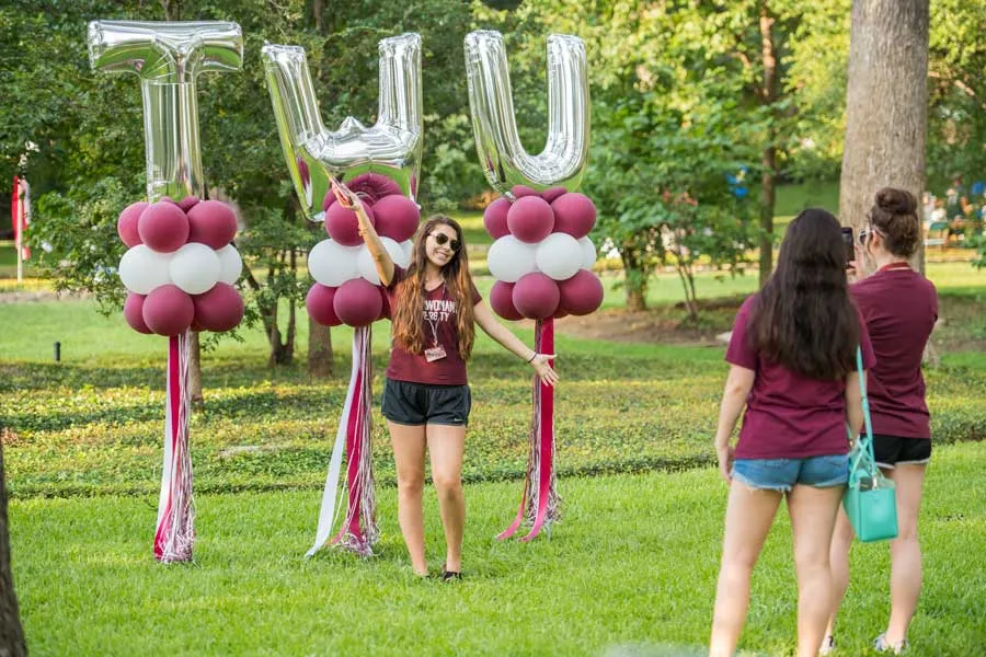 A TWU student poses in front of large balloons in the shape of TWU letters.