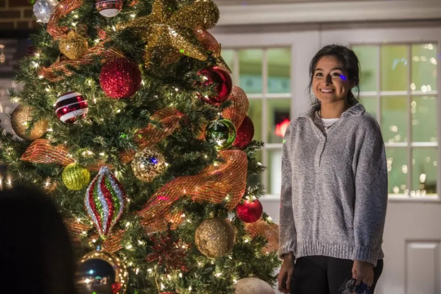 A TWU student posing next to a tree decorated with ornaments, lights, and ribbons.