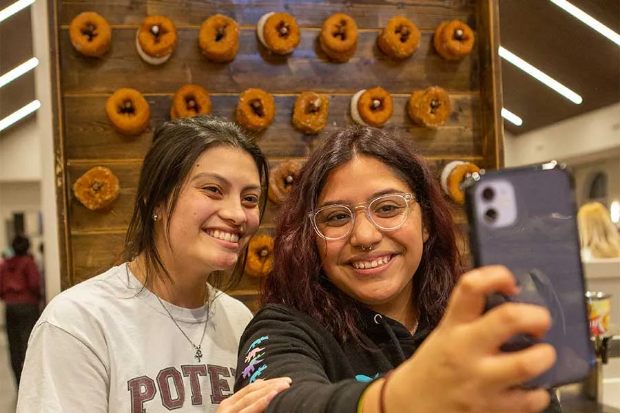 TWU students take a selfie in front of a donut wall in the Denton campus dining hall.