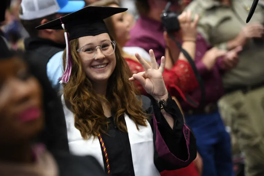 A graduate at her commencement ceremony holding up the TWU hand sign.