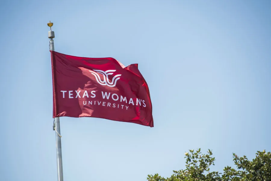 A maroon flag flying on TWU's Denton campus with the logo in white.