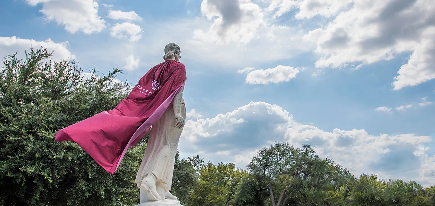 The Pioneer Woman statue on the Denton campus wearing a long cape with the TWU logo on it