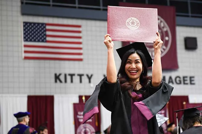 A TWU graduate holds up her diploma and smiles