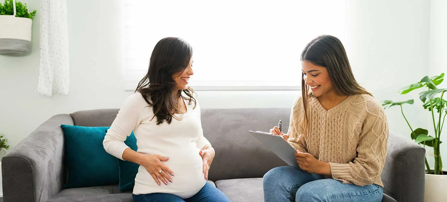 A doula sits in an office setting with a pregnant patient and takes notes.