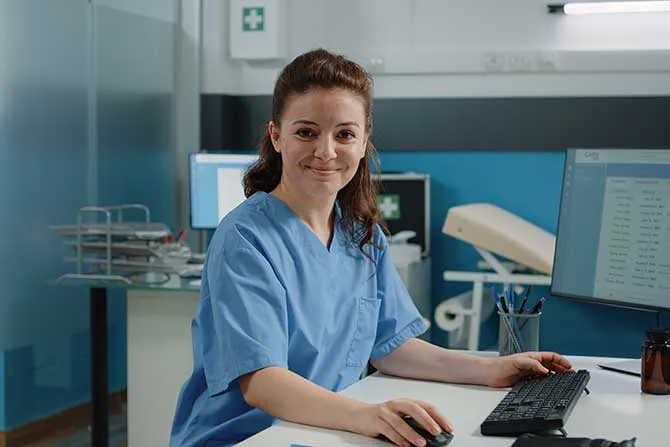A medical assistant works at a computer in a hospital setting.