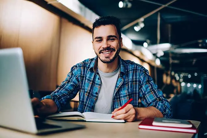 A man studies at a computer with notebooks open.
