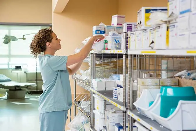 A woman in scrubs searches for medical supplies in a storage area.