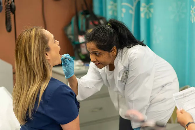 A healthcare student uses a tongue depressor on a patient to check the back of their throat