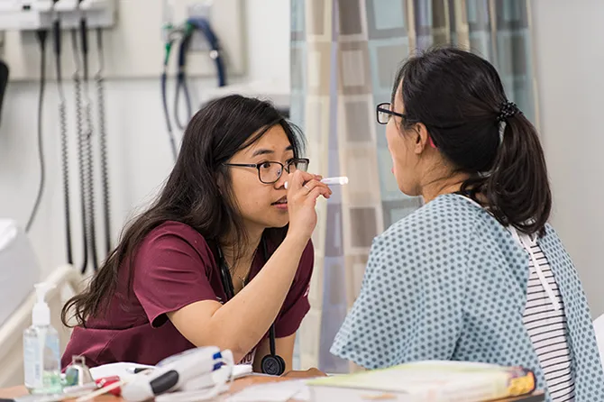 A student uses a pen light to check a patient's throat