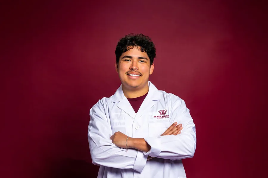 A young man wearing a white lab coat with the TWU logo embroidered on it