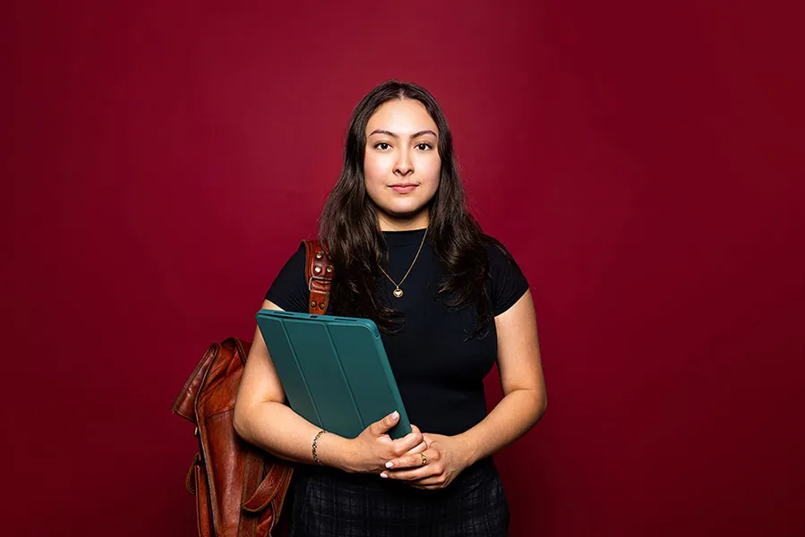 A young woman wearing a leather backpack and holding a computer tablet