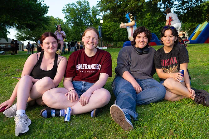 A group of four TWU students relax on the Hubbard Hall lawn at an event.