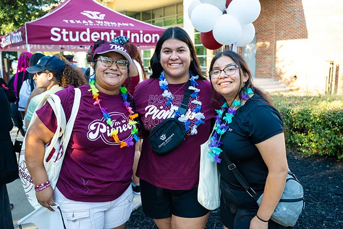 Three TWU students smile and pose for a photo at a campus event.