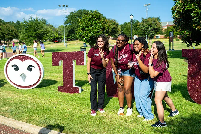 Four TWU students all wearing maroon take a photo next to a giant Oakley sign.
