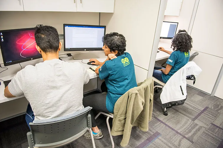 A Write Site tutor assists a student with their essay in a computer lab.